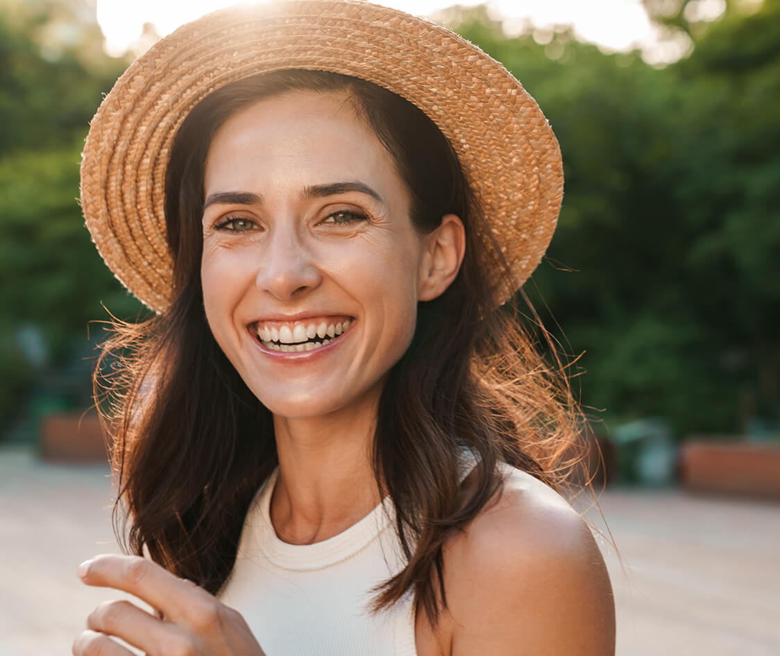 Image of beautiful middle-aged woman laughing and looking at camera while walking in summer park