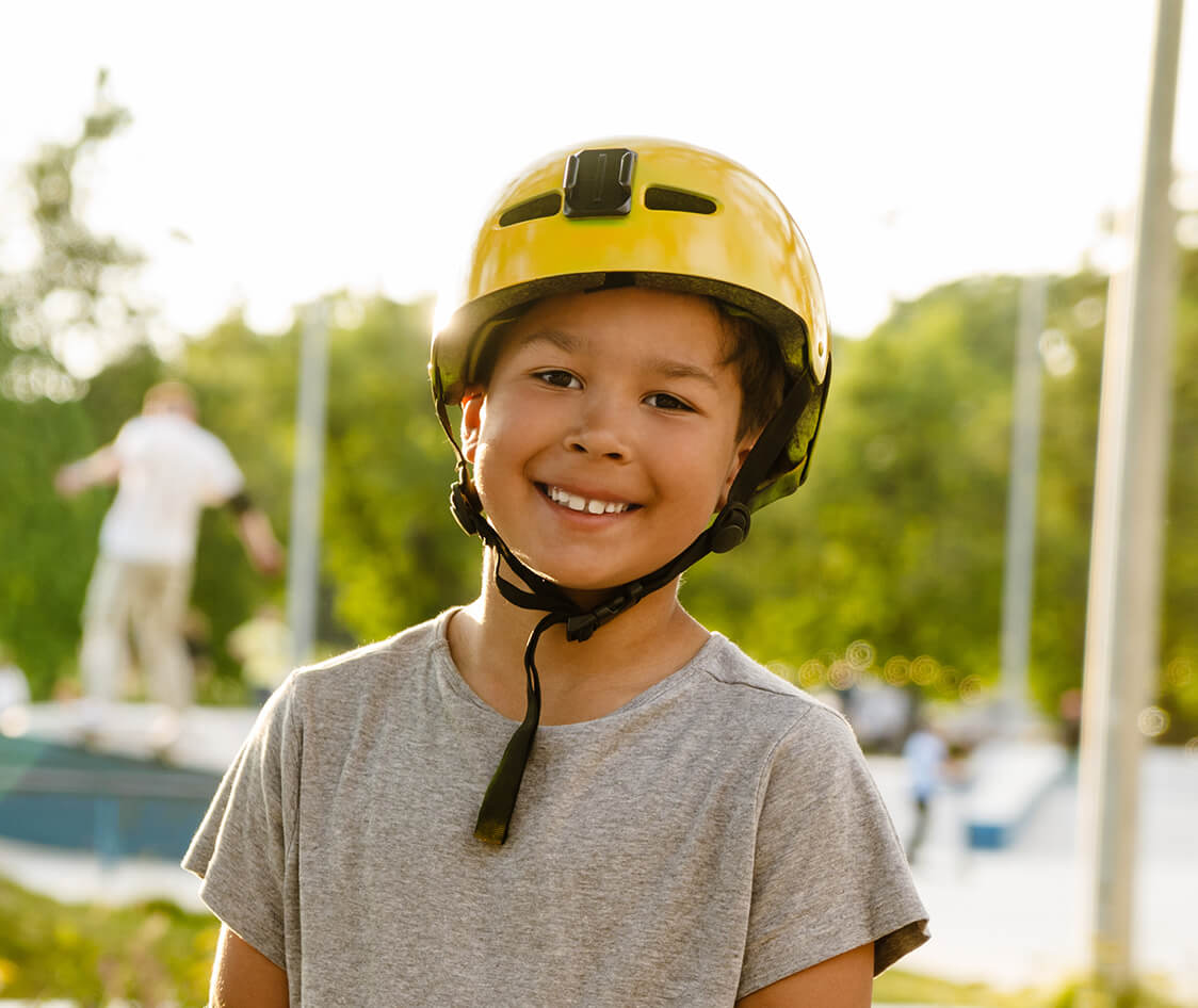 Smiling boy wearing safety helmet holding skateboard while standing in park